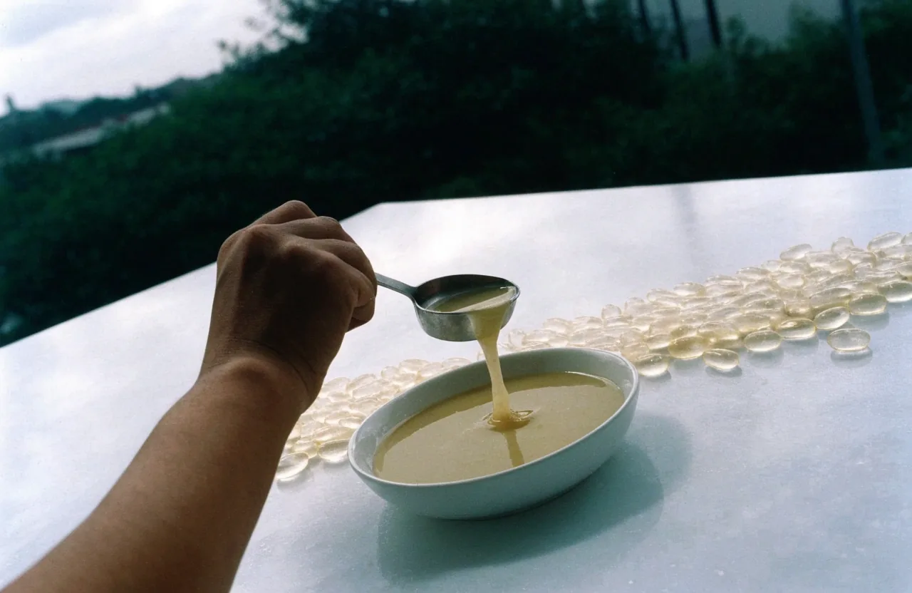 A Yogyakarta compounding counter in overcast north light, with extract granules in a steel dish and hands sorting empty capsule halves
